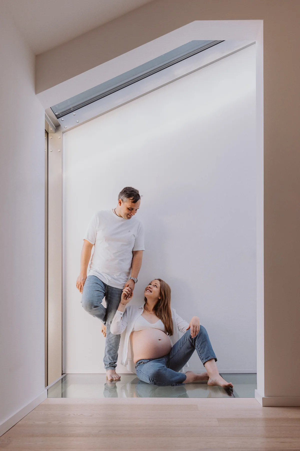 Werdende Eltern sitzen Hand in Hand auf einer hellen Treppe